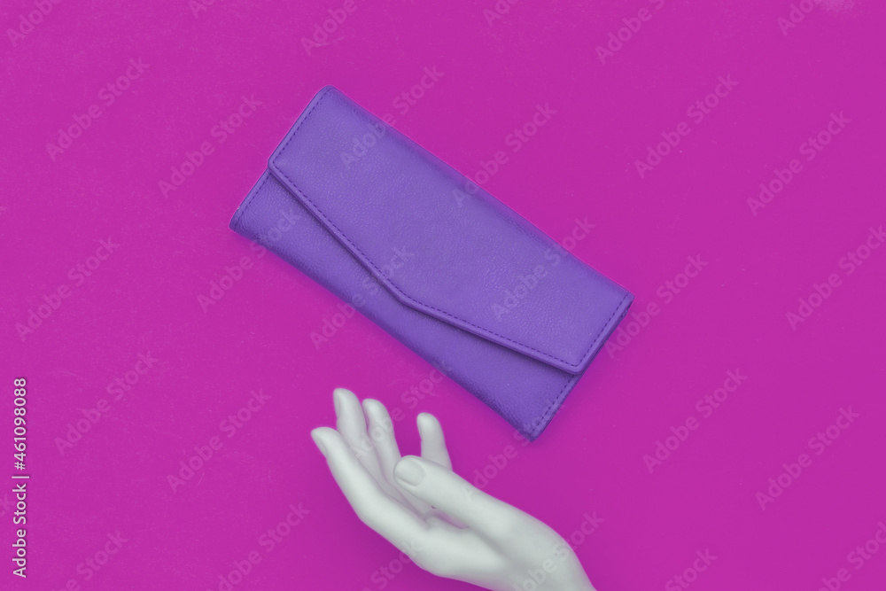 The mannequin's white hand touches leather wallet on pink background. Top view The mannequin's white hand touches leather wallet on pink background. Top view