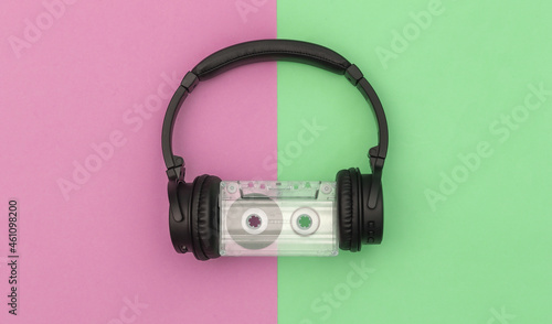 Stereo headphones with retro audio cassette on pink green background. Top view