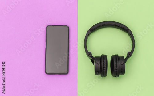 Wireless stereo headphones and smartphone on pink green pastel background. Top view