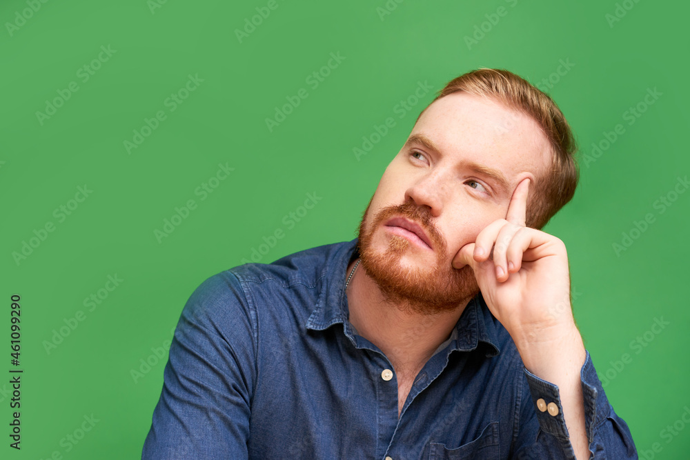 Serious redhead young man with beard sitting against green background and being deep in thoughts Serious redhead young man with beard sitting against green background and being deep in thoughts
