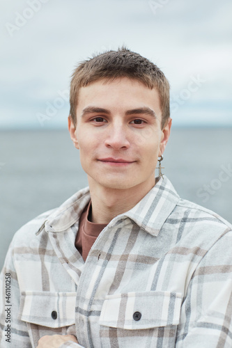 Vertical portrait of smiling young man looking at camera on beach with sky in background