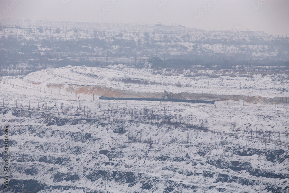 Iron ore quarry horizons covered with snow in winter, mining process in winter in cloudy weather
