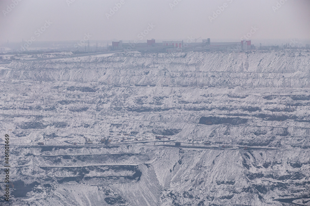 Iron ore quarry horizons covered with snow in winter, mining process in winter in cloudy weather