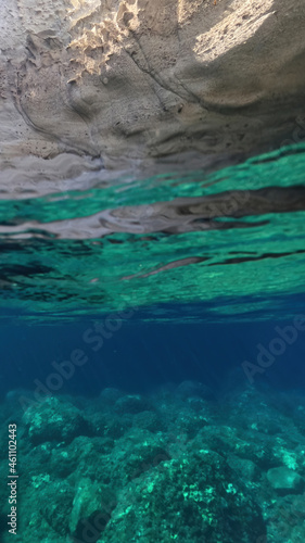 Underwater split photo of beautiful deep turquoise cave of Sykia a natural volcanic white chalk round shaped open top bay, Milos island, Cyclades, Greece