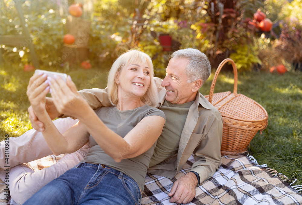 Modern elderly spouses taking selfie on smartphone, having picnic and resting in garden at sunny autumn day Modern elderly spouses taking selfie on smartphone, having picnic and resting in garden at sunny autumn day