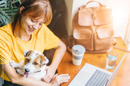 Young woman working with laptop and hugging her cute Jack Russell Terrier at home. Lovely pet concept. photo