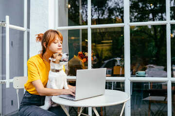 Lovely pet concept. Girl work with laptop, plays with a dog. Redhead woman hugging with dog at cozy cafe outdoor. Shelter a mongrel at home. Life style. College People Study Learning Reading Notes.