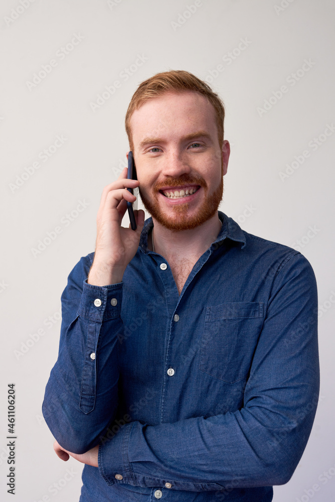 Portrait of cheerful young red-bearded manager in dark blue shirt communicating by mobile phone Portrait of cheerful young red-bearded manager in dark blue shirt communicating by mobile phone