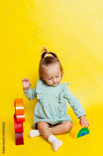 Portrait of a cute baby girl with blue eyes on a yellow background  playing with a rainbow designer. educational games and toys. Teaching the child. Color. A place for text.