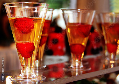 Yellow transparent cocktail with red strawberries in narrow triangular glasses, blurred background © Natalya