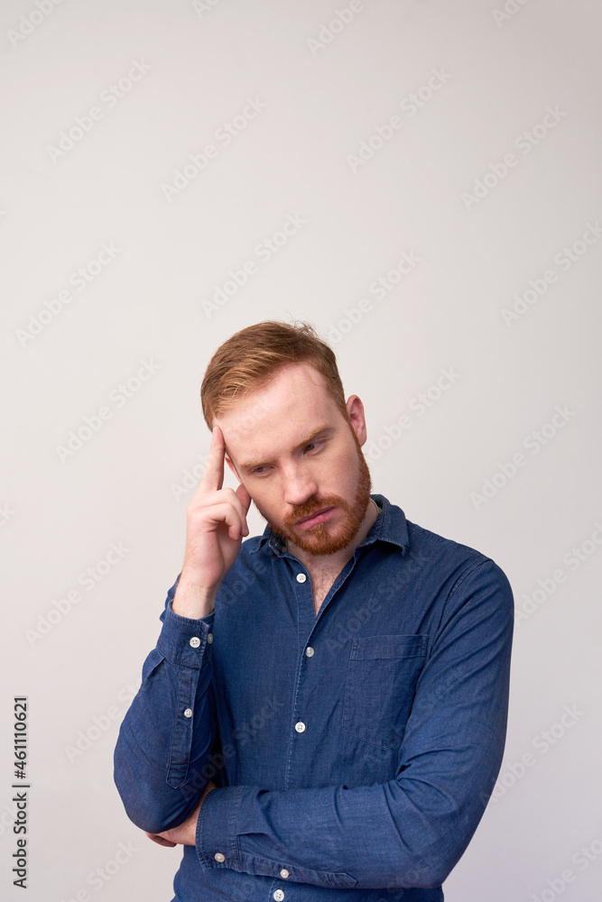 Serious young redhead man with beard focused on thoughts touching forehead against gray background Serious young redhead man with beard focused on thoughts touching forehead against gray background
