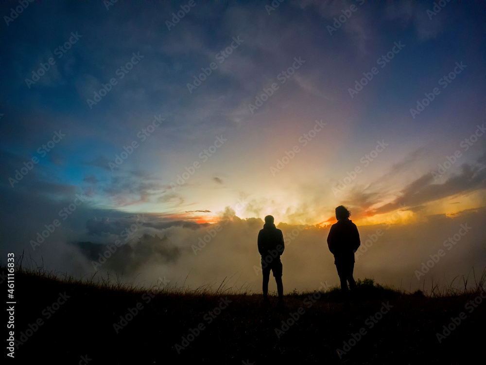 Silhouettes of two campers watching the sunrise in the mist from top of 'Le Pouce' mountain