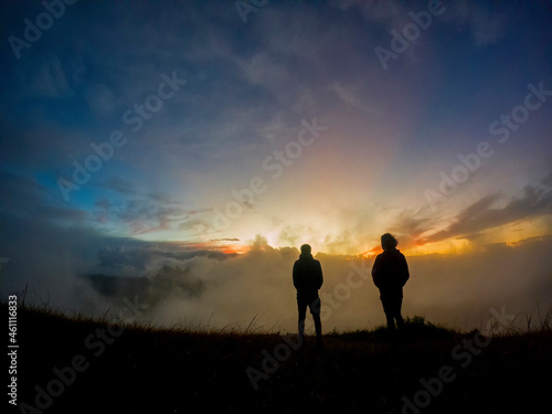 Silhouettes of two campers watching the sunrise in the mist from top of  Le Pouce  mountain
