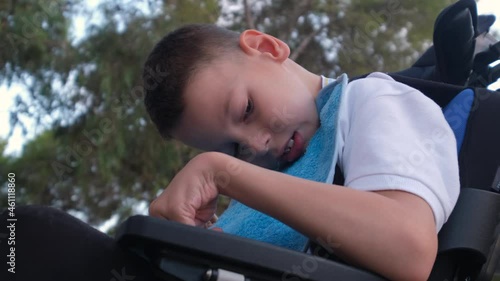 Little 9s boy with cerebral palsy sit in wheelchair outdoor, close up view photo