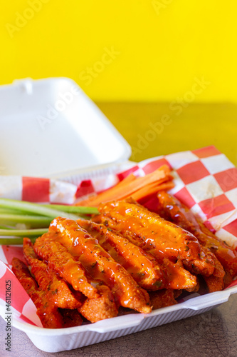 Tiras de pollo tipo tenders con salsa búfalo y vegetales con fondo amarillo