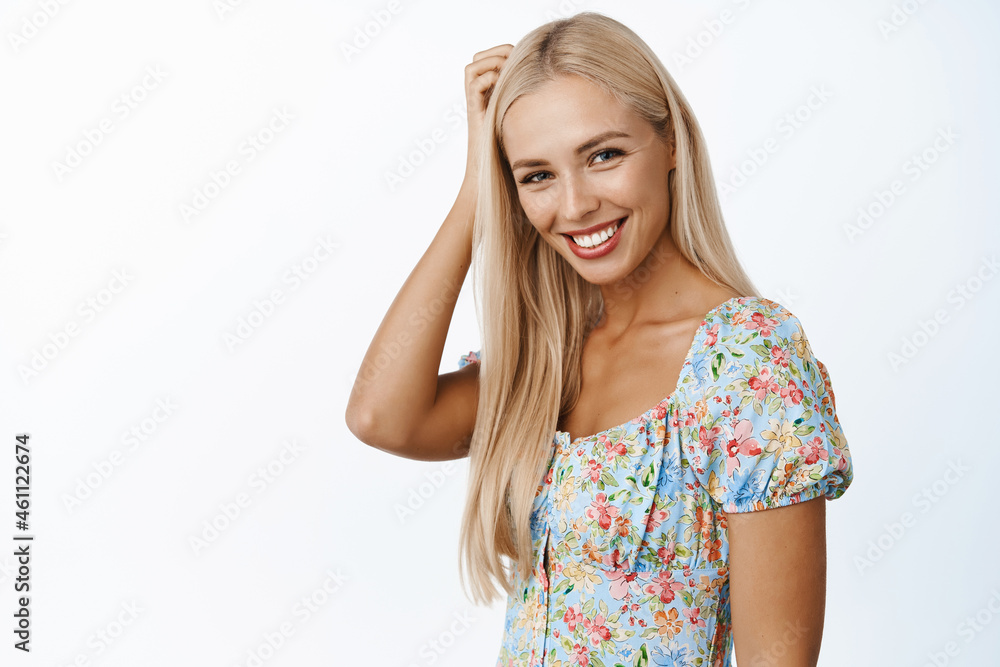 Skin care and beauty. Beautiful blond girl gazing at camera, smiling flirty, standing in dress against white background Skin care and beauty. Beautiful blond girl gazing at camera, smiling flirty, standing in dress against white background