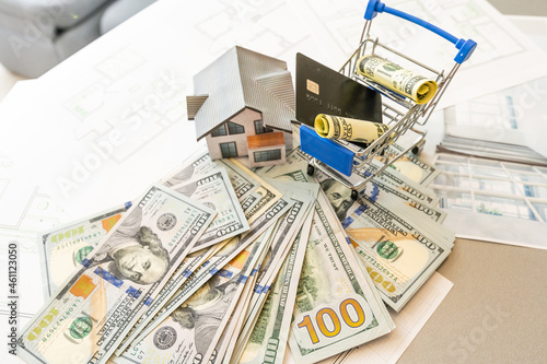 Miniature model of house against the background of a house plan, and money, and calculator.