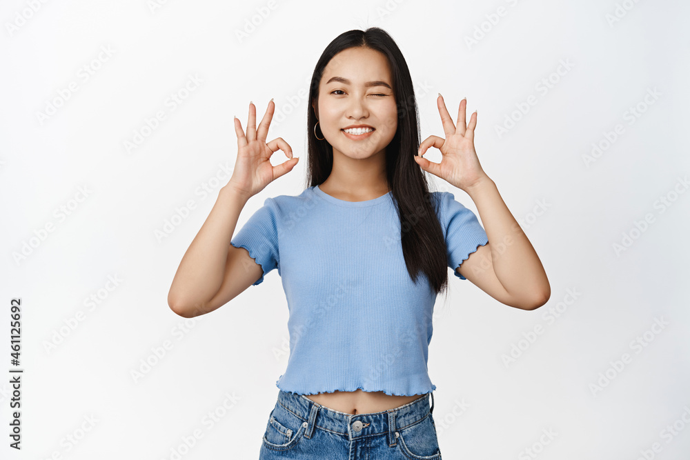 Cute asian girl winking and smiling, showing okay, ok zero gesture, confirm something is good, recommending product, white background