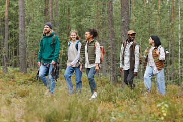 Diverse group of young people walking in forest with backpacks while exploring hiking trails, copy space