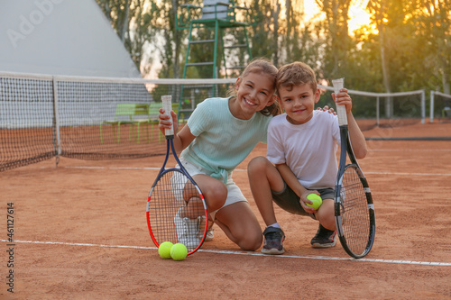 Cute children with tennis rackets and balls on court outdoors © New Africa