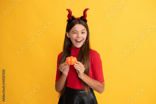 happy halloween. devil kid with pumpkin. trick or treat. teen girl on yellow background.