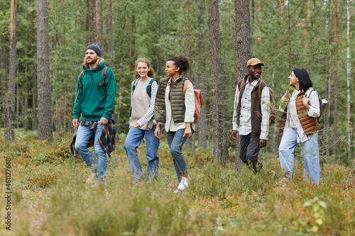 Diverse group of young people walking in forest with backpacks while exploring hiking trails, copy space