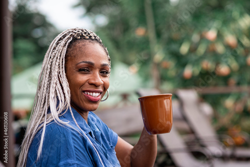 Mujer madura afroamericana con cabello con trenzas sonriendo mientras bebe un café photo