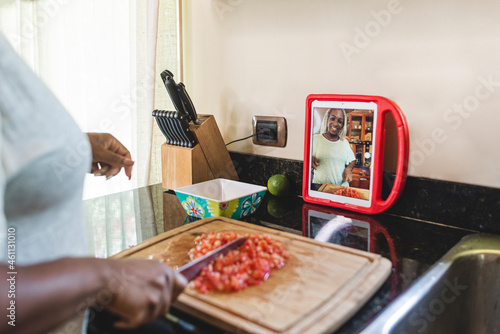 Mujer afroamericana en la cocina picando tomate y haciendo una transmisión en vivo por las redes sociales photo