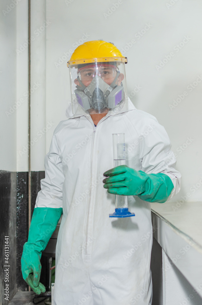 Industrial man worker in white protective overalls goggles, mask and face shield holding a test tube in an asphalt testing laboratory Industrial man worker in white protective overalls goggles, mask and face shield holding a test tube in an asphalt testing laboratory