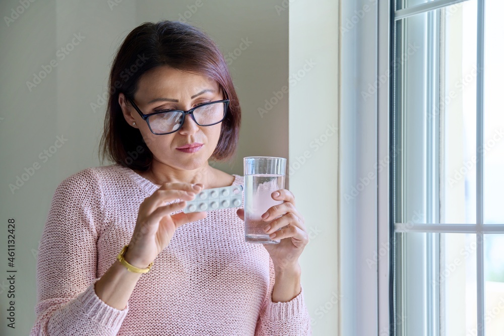 Middle-aged woman with pills and glass of water in her hands, at home Middle-aged woman with pills and glass of water in her hands, at home
