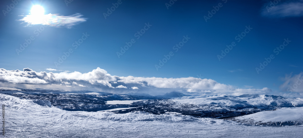 Very scenic panorama view at Scandinavian Mountains, ski slope with lot of traces. No people yet, Sunny day , much snow and blue skies with fluffy clouds, strong Sun