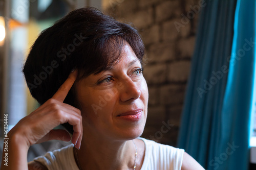 Close-up portrait of a pensive pretty Jewish woman against the background of a brick wall in a cafe under electric light.