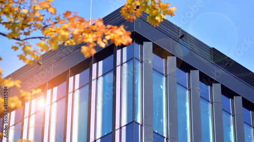 Inspiring view of the modern city. The wall of the building of glass and metal against trees. Corporate construction and ecology, view of  modern  building with blue sky and green tree. Sunlight