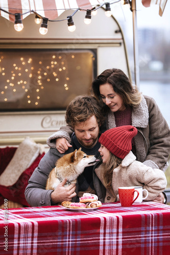 Joyful family bonding outside camper car travelling or camping in forest together on Christmas vacation. Young parents enjoy relaxing winter weekend on New Year with daughter and cute dog outside city