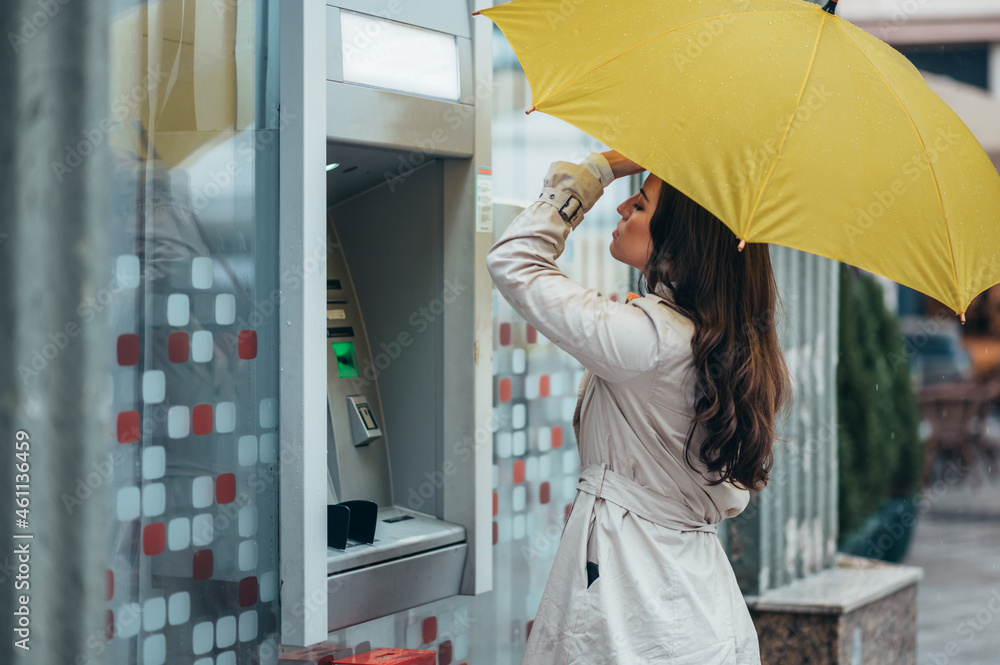 oman holding a yellow umbrella while using the atm machine oman holding a yellow umbrella while using the atm machine