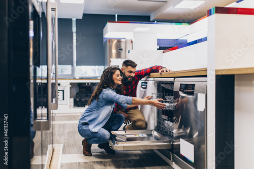 Beautiful and happy young couple buying dishwasher in modern appliances store.