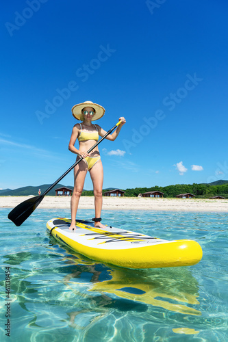 Tanned tourist female in straw hat standing on surfboard with paddle enjoying sup surfing photo