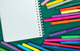 Multicolored markers or felt-tip pens and notepad on the green background.