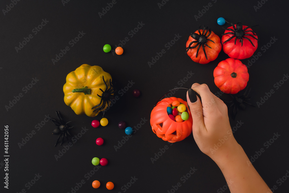 Hands with manicure hold a basket of Halloween sweets. Background with pumpkins and spiders