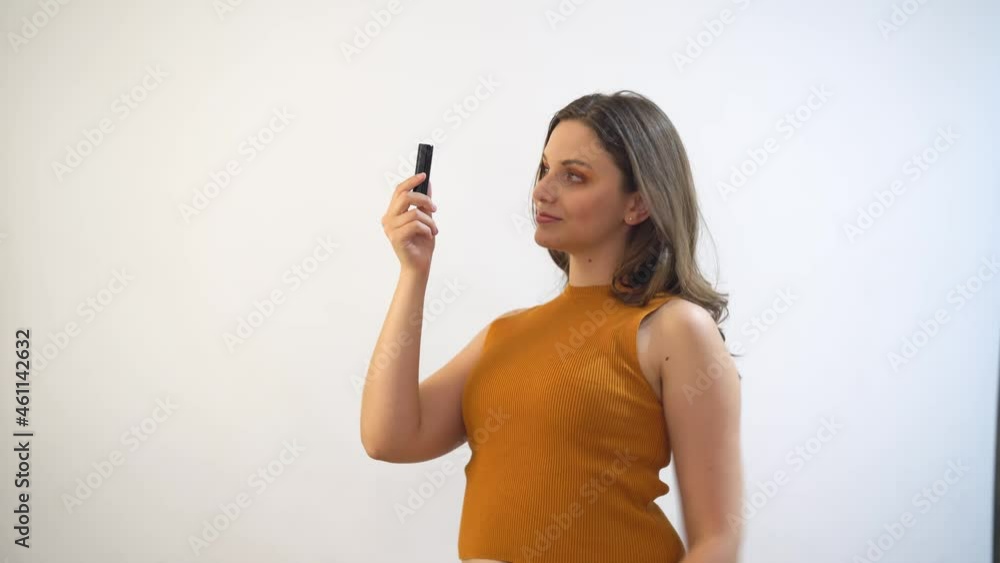 Young pretty female looking at red lipstick and wearing it while smiling to camera Young pretty female looking at red lipstick and wearing it while smiling to camera
