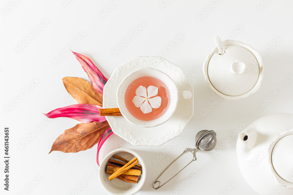 Tea time pale pink composition with a cup of tea with a white flower inside, pink and brown leaves, tea pot, cinnamon on white background. Flat lay, top view. Copy space. Tea time pale pink composition with a cup of tea with a white flower inside, pink and brown leaves, tea pot, cinnamon on white background. Flat lay, top view. Copy space.