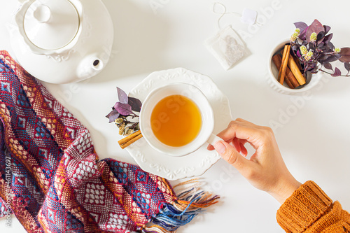 Woman's hand holding a cup of ginger tea composition with  purple and pink leaves, cinnamon, tea strainer, tea bag on white background. Flat lay, top view. Tea time concept. photo