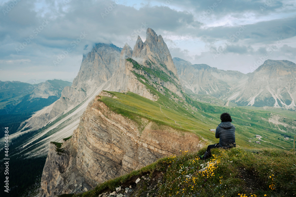 Man from behind sitting on the cliff of Seceda mountains.