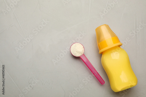 Feeding bottle with infant formula, scoop of powder and space for text on grey table, flat lay. Baby milk © New Africa
