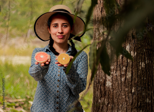Peasant woman in Latin America, showing two halves of an orange in her hand. two halves of orange with different color. choose. One orange and one yellow. varieties of oranges in Latin America.