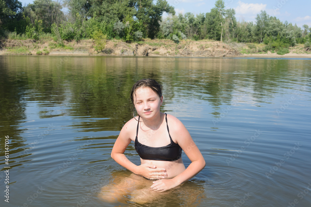 Girl teenager sits in water of the river summer beach. Abdominal pain from bathing in dirty water Girl teenager sits in water of the river summer beach. Abdominal pain from bathing in dirty water