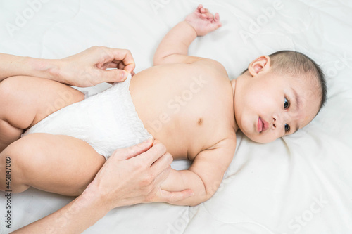 Mother's hand taking care of little boy. Mom giving baby a diaper change on bed.