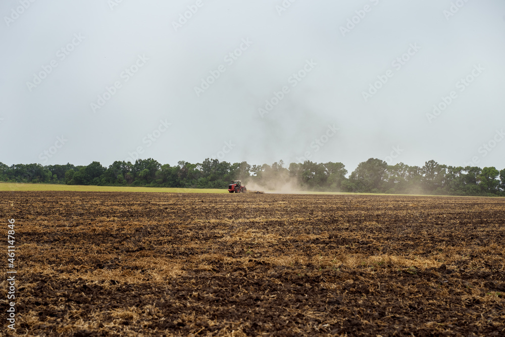 Fototapeta premium The tractor plows the field against the background of the sky. Harvesting in the field. Autumn work on the farm. Mechanized work. Modern farming.
