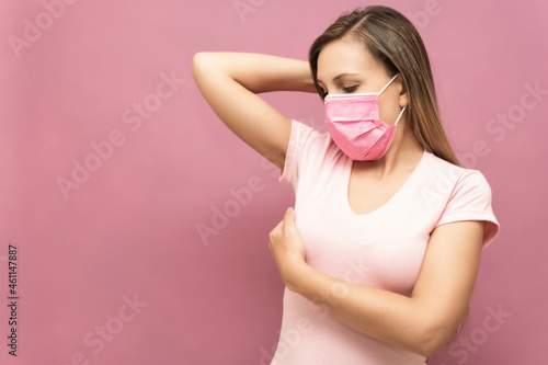 young woman does self-exam for breast cancer prevention wearing face mask in front of a pink background. High quality photo