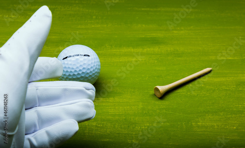 Obraz na płótnie Hand with white golf glove with ball and small wooden support to hold the ball on the grass